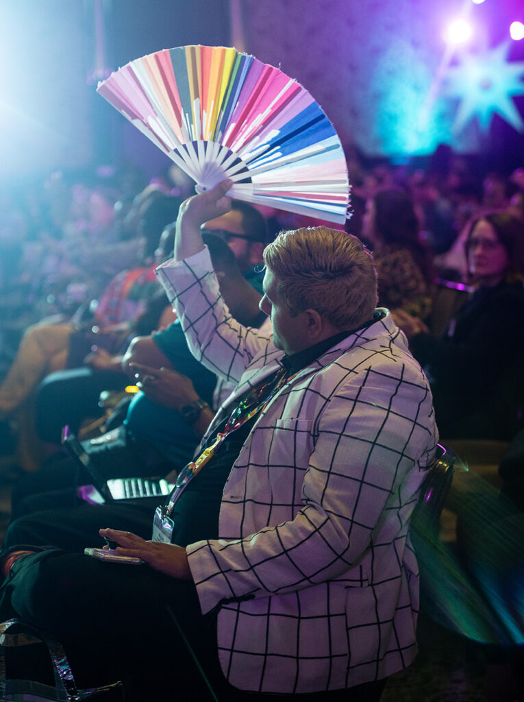 A man in a brightly colored jacket holding up a rainbow flag.